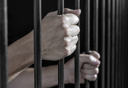 Prisoner's hands gripping the bars of a cell in jail